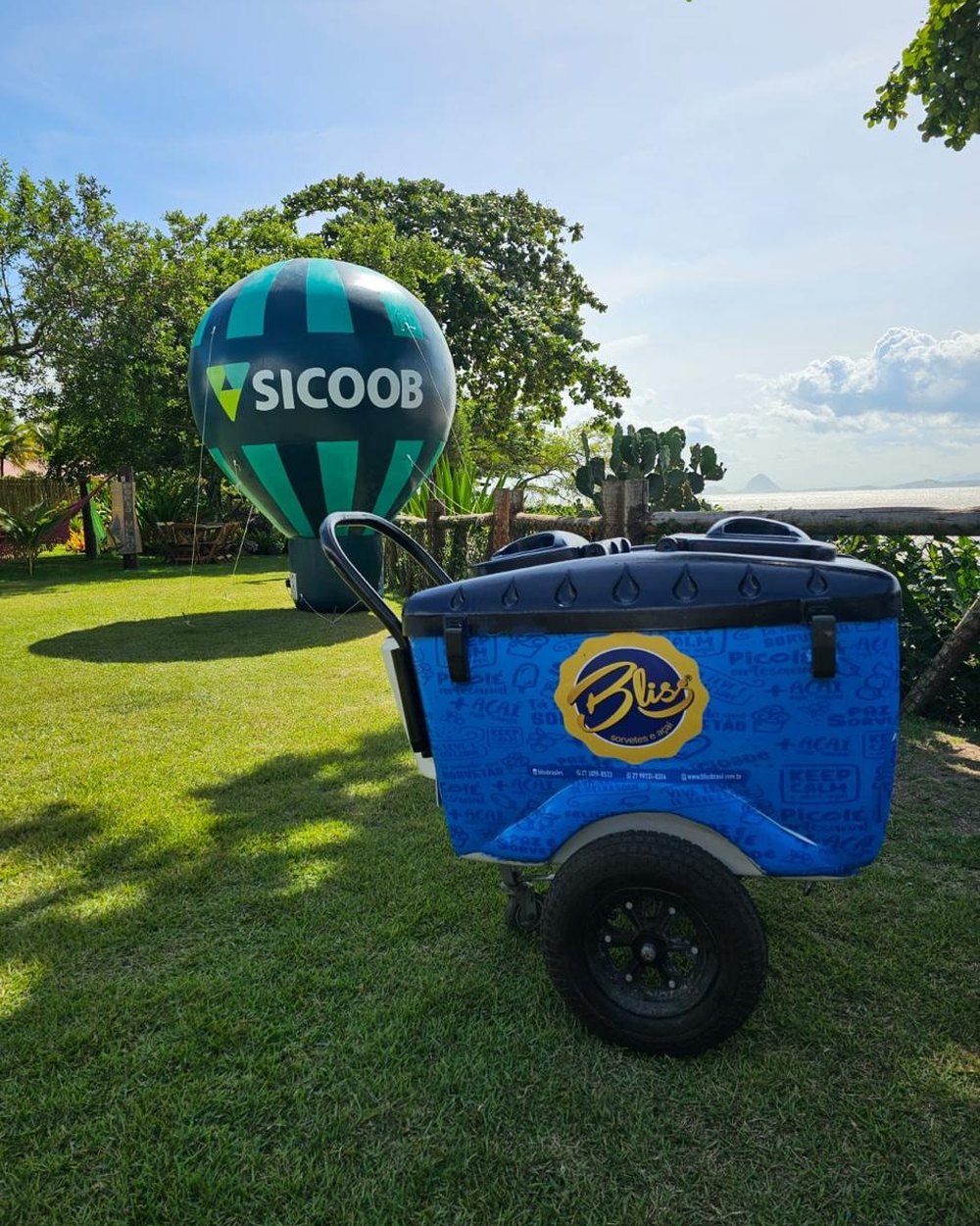 Carrinho Bliss montado em gramado à beira-mar, ao lado do balão do Sicoob