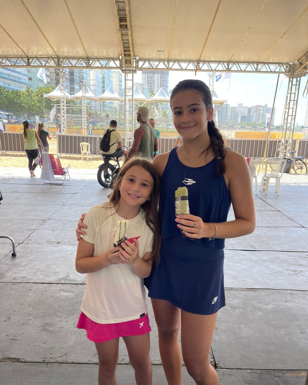 Duas jovens atletas de beach tennis segurando picolés Bliss embaixo da tenda do evento