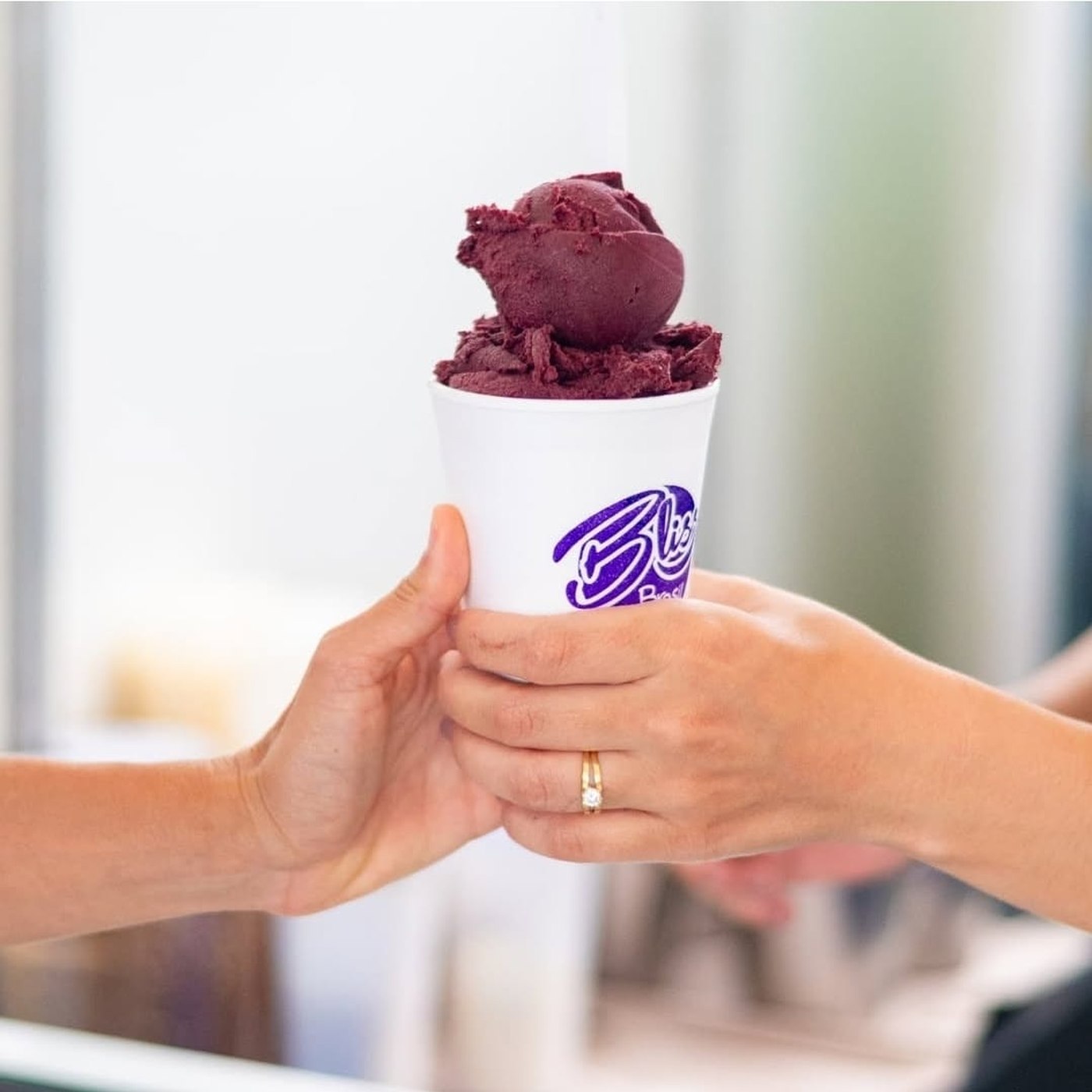 Copo de açaí Bliss sendo entregue de mão em mão
