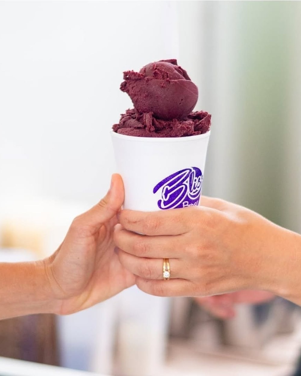 Copo de açaí Bliss sendo entregue de mão em mão