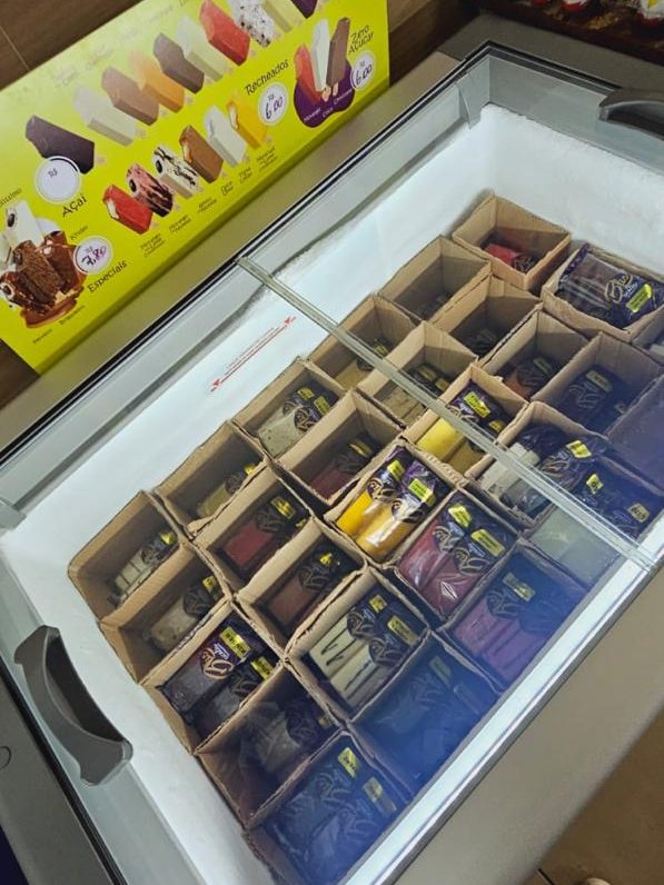 Freezer Bliss aberto em ponto de venda parceiro, com as caixas de cada sabor organizadas e a tabela de sabores ao lado